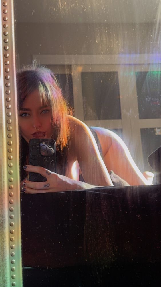 Tattooed girl taking a picture of herself in the mirror on her bed
