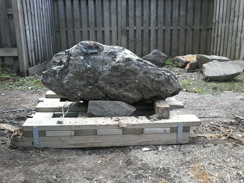 A photo of a homemade rock sled that's about 3.5-4 feet long and has two rocks (one large, one small) sitting on top.