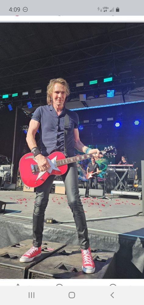 Rick Springfield in concert appreciating  his front row audience as he smiles for the camera.