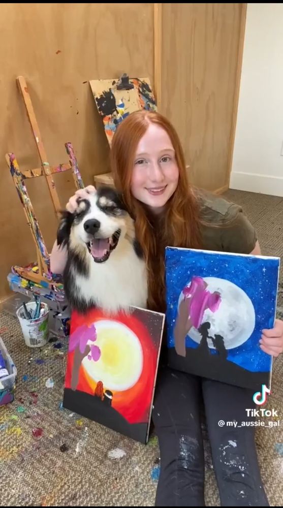 Woman shows the paintings her and her dog made together. 