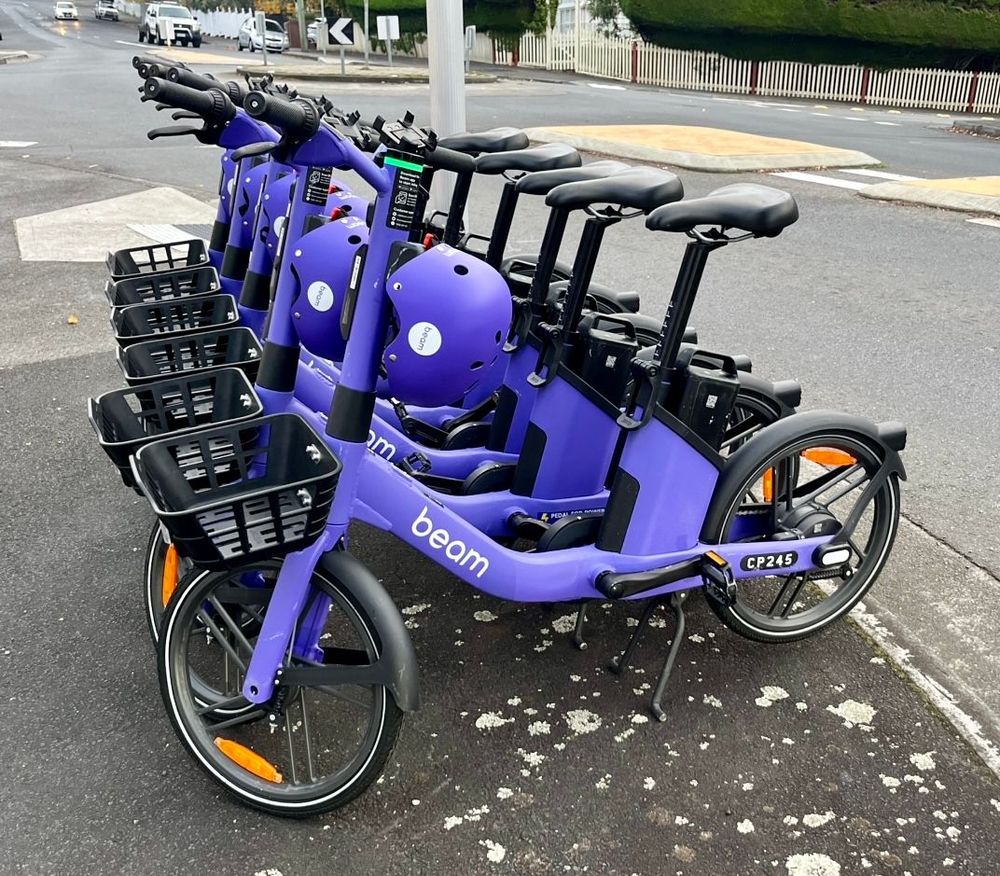 Several purple electric bikes with the brand name “Beam” parked beside a street