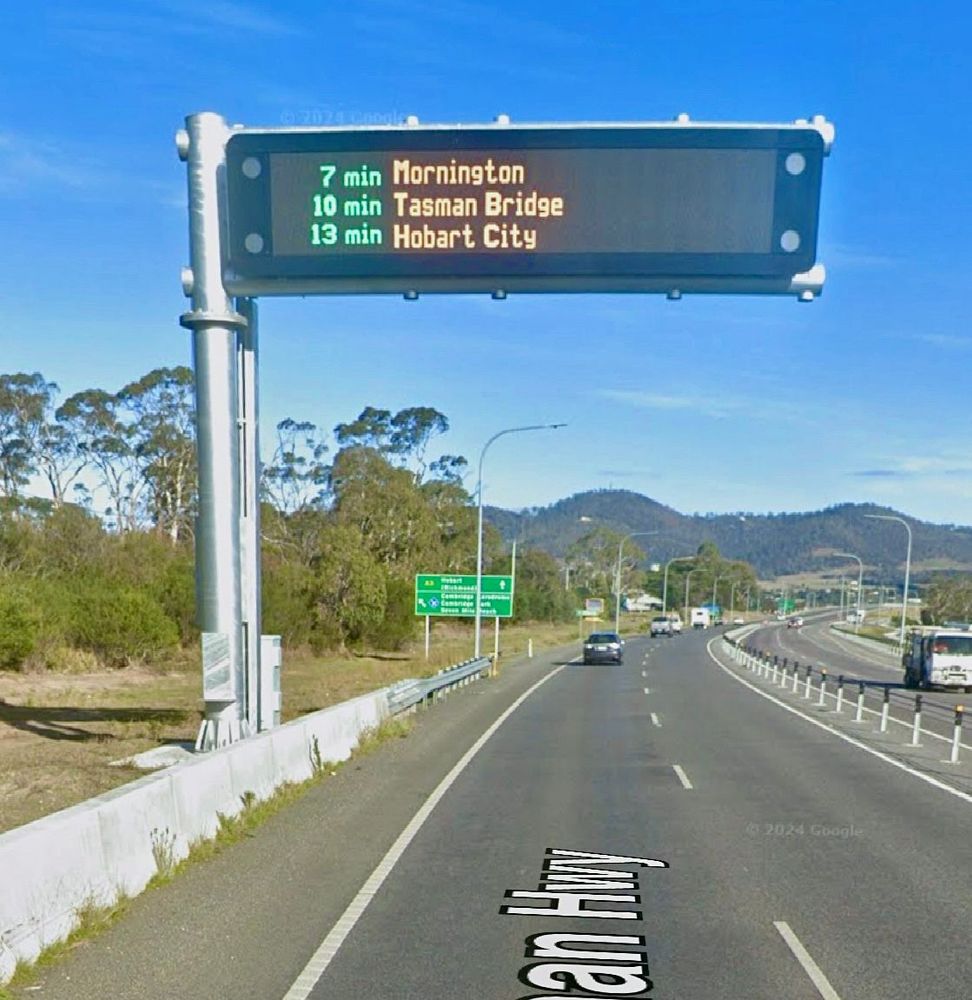 A large overhead sign on the Tasman Highway near Hobart Airport displaying current travel times to Mornington (7 min), Tasman Bridge (10 min) and Hobart City (13 min).