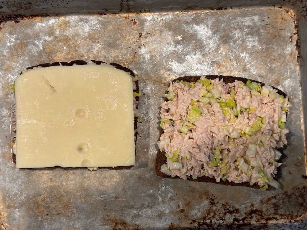 An overhead picture of tuna melt being made. One half of it has a piece of cheese that is exactly the same size as the bread.