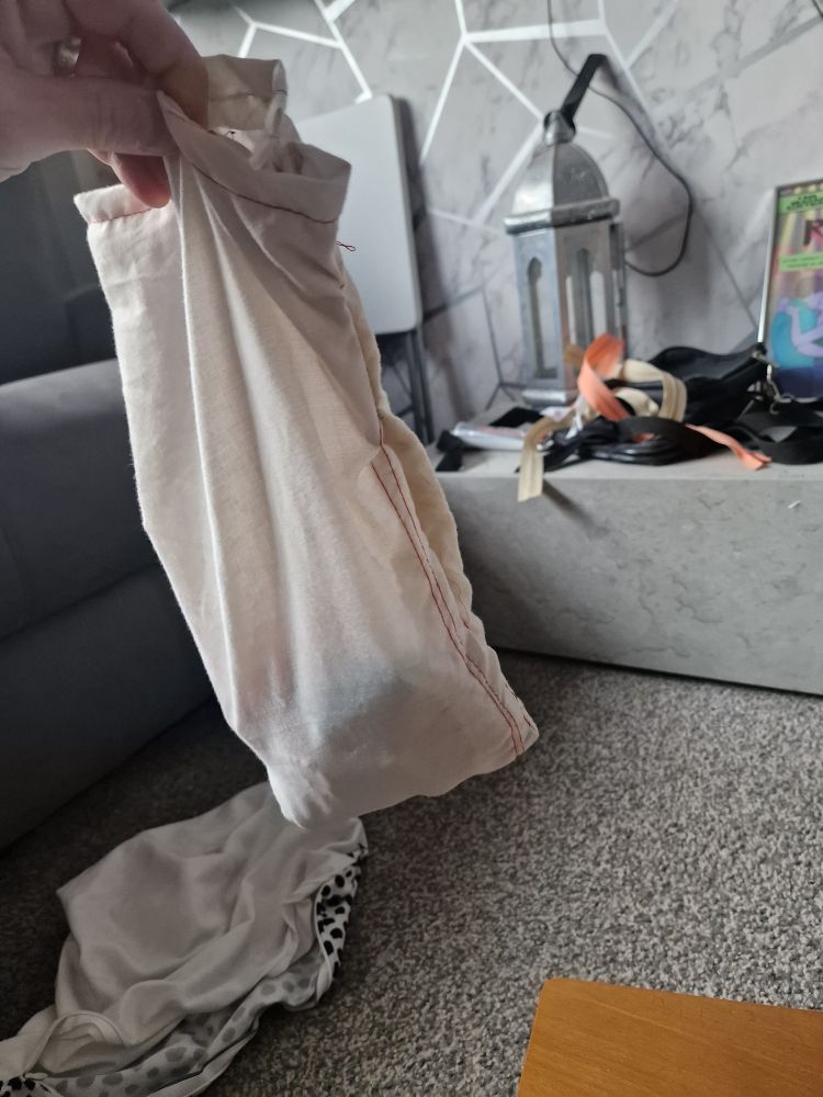 This image shows a person's hand holding up a light-colored, off-white cloth bag or pouch.