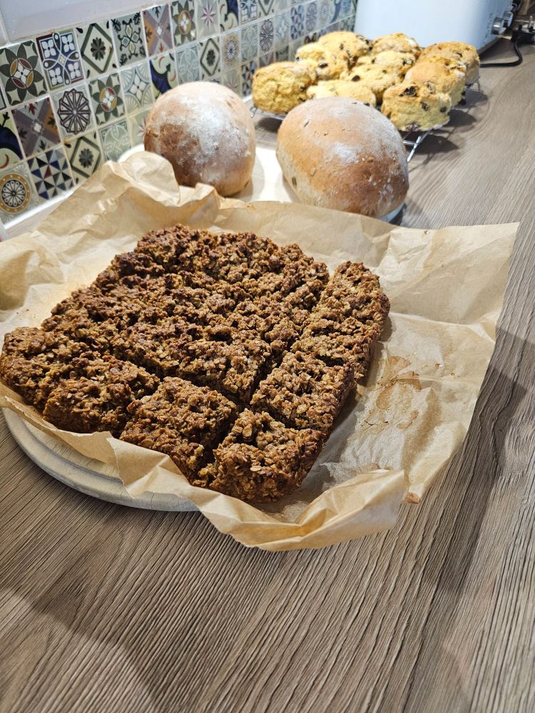 Homemade flapjacks, fruit scones and seeded bread loaves cooling on racks.