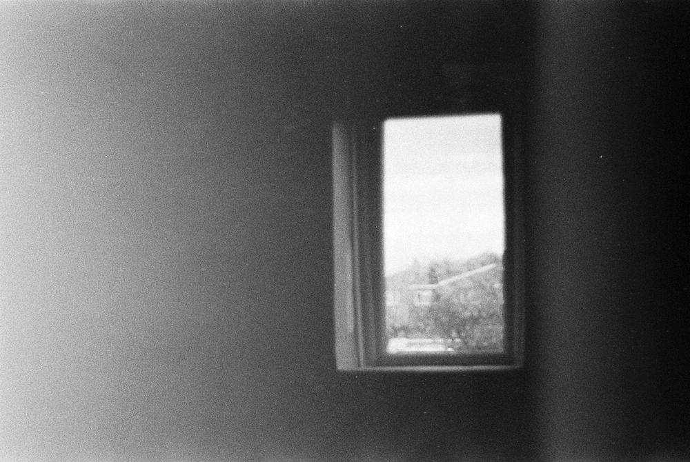 grainy black and white photo of a small window. a major light leak is creeping in from the left