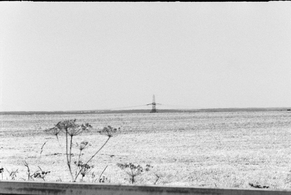 a grainy black & white photo of a field. an electricity pylon is in the distance, small against the sky 