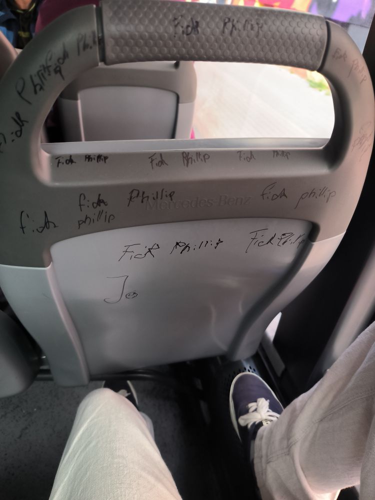 Ein Bussitz von hinten, auf den mit einem dünnen Edding mehrere Male "Fick Phillip" geschrieben wurde. Scheinbar hat der Bus gewackelt, als die Nachricht geschrieben wurde, denn die Buchstaben sind krumm und schief