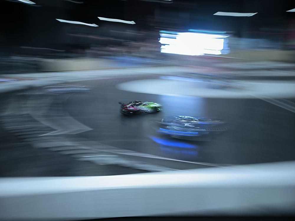 Insgesamt drei ferngesteuerte Driftautos auf einem kleinen Track. Das Foto ist von außen geschossen, sehr verschwommen und richtig erkennen kann man nur eins der drei Autos