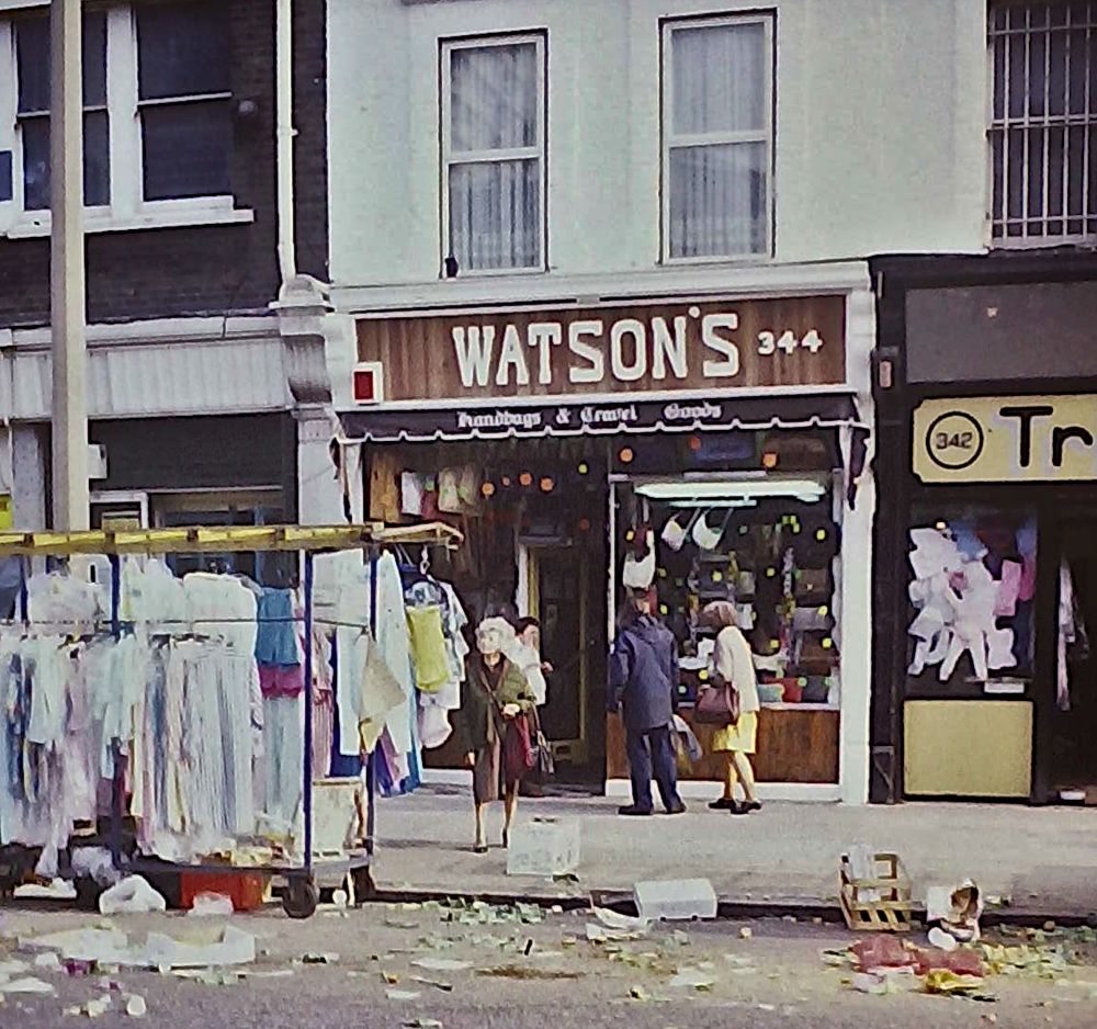 Street scene, with the 'WATSONS' shop partially obscured by a market stall. Lots of rubbish in the gutter.