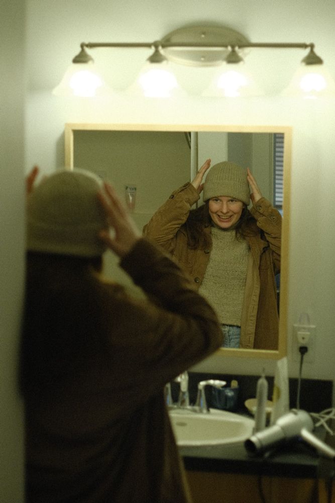 Photo of me trying on my newly knit Classic Ribbed Hat by Purl Soho in my messy bathroom. I'm facing away from the camera but you can see me in the mirror.