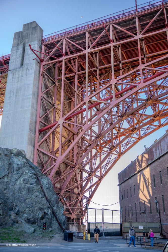 Golden Gate Bridge superstructure and part of the Fort Point building. People walking and looking at the sites. 