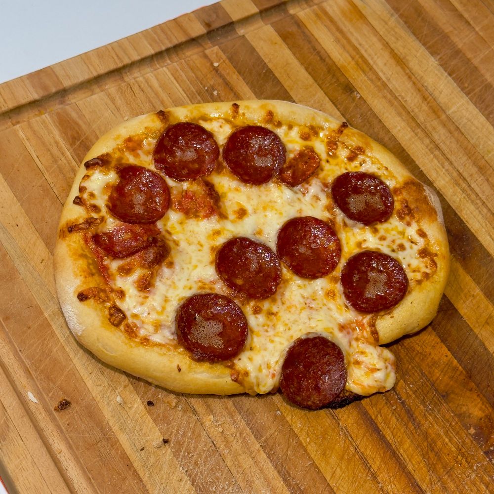 Homemade pizza with pepperoni. One edge of the pizza was too low and melted cheese oozed out. The pizza is roughly 12 inches in diameter. 