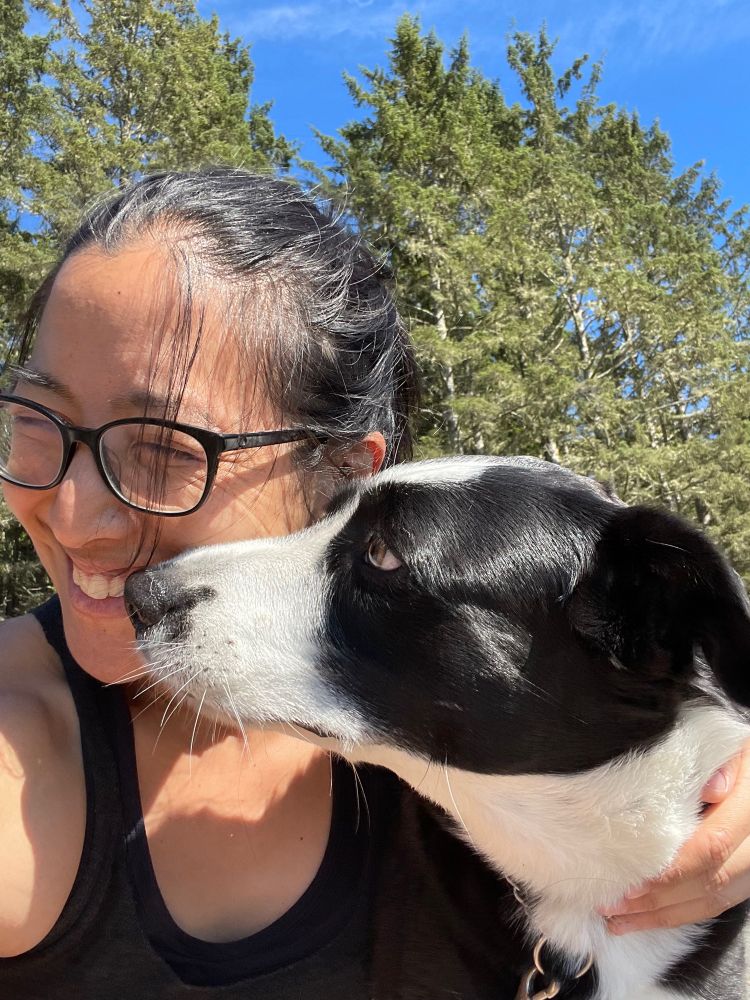 It’s me laughing with trees in the background trying not to let a border collie stick her tongue in my mouth