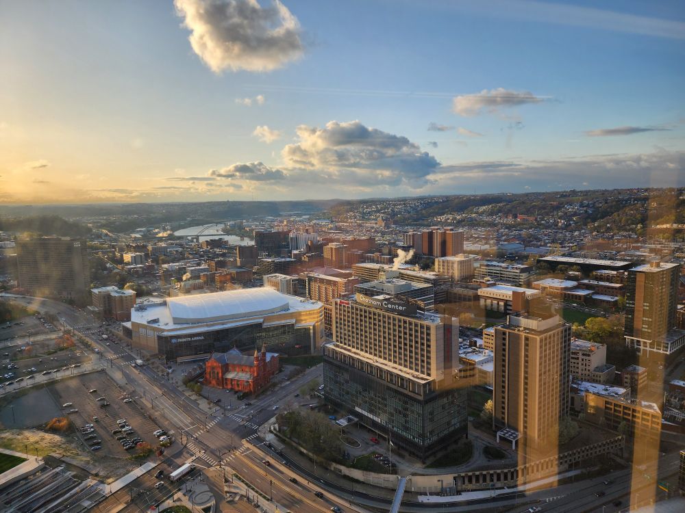 The sky is sunny and blue with some puffy white clouds. The picture is taken from the U.S. Steel Tower facing east overlooking the neighborhoods of Uptown and Southside.