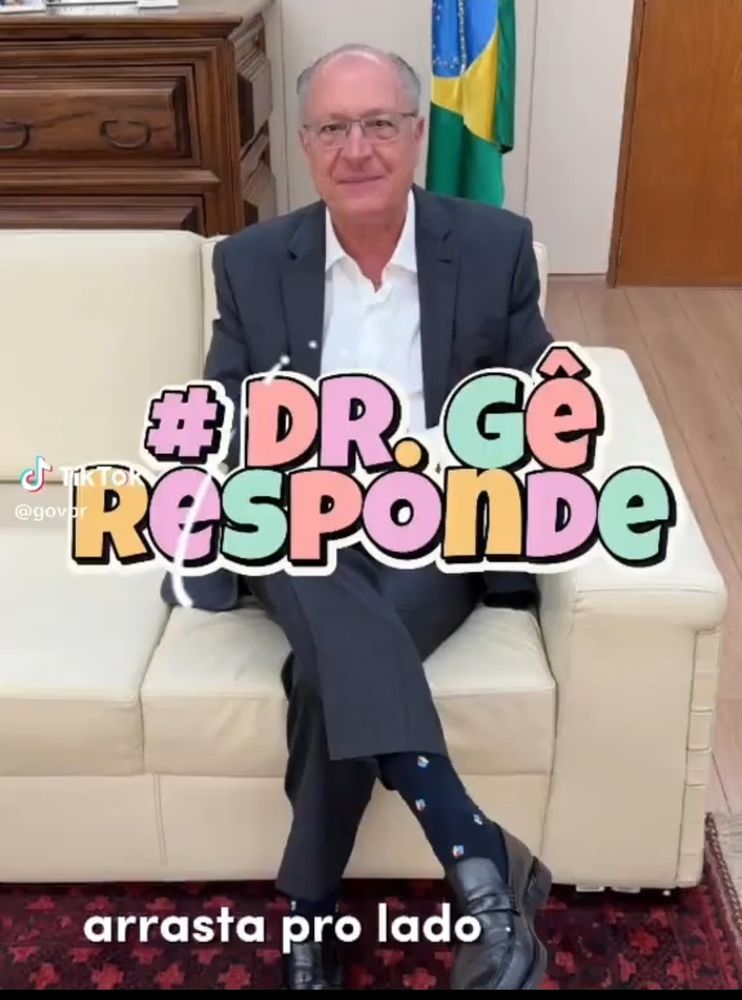 Foto de Geraldo Alckmin sentado num sofá creme com a bandeira do Brasil de fundo. No centro do vídeo uma legenda #Dr.Gê responde em tons pastel 