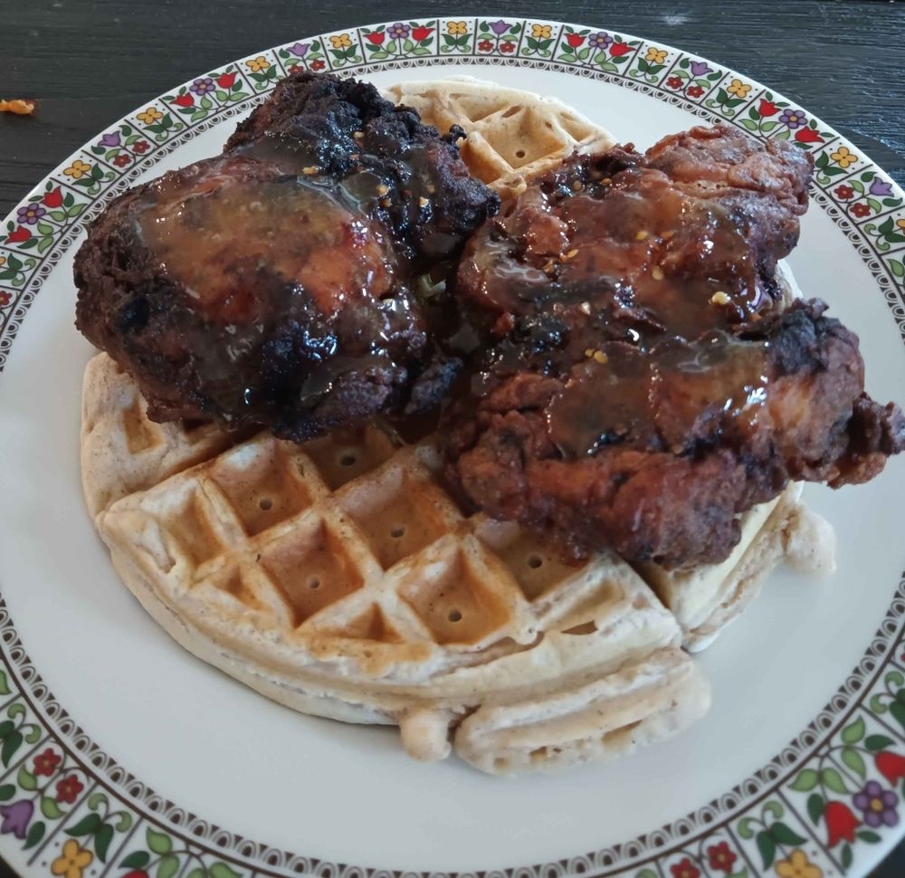Plate with two fried chicken thighs stacked on top of a waffle, topped with a honey sauce.