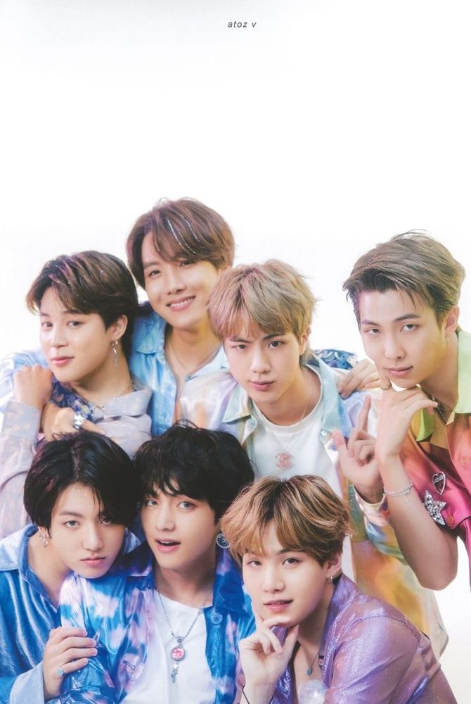 Photo of BTS wearing holograpgic colorful shirts. J-hope is in the back center with his arms around
Jimin and Jin. RM is next to Jin poking his cheek. In the front, Jungkook has his chin on V's shoulder and Suga is next to them head resting on his hand.