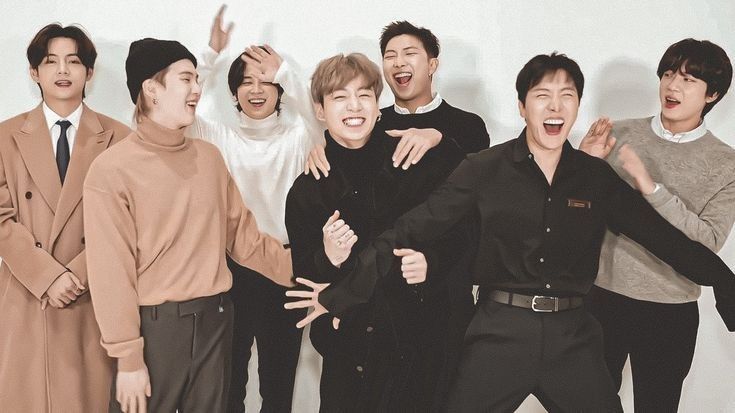 Photo of the BTS member's laughing. They are in front of a white wall and wearing coordinating black, white, and tan outfits. Left to right: V, Suga, Jimin, Jungkook, RM, J-hope, and Jin.