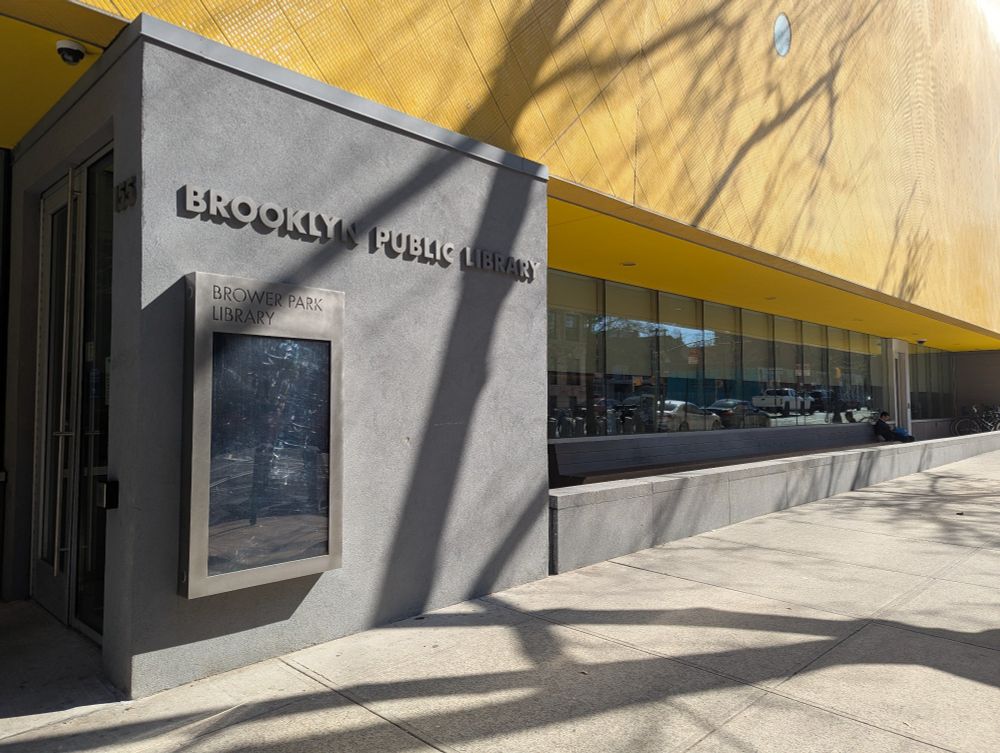 The entrance to the Brower Park branch of the Brooklyn Public Library. A bright yellow second story sits above a concrete entrance and tall windows