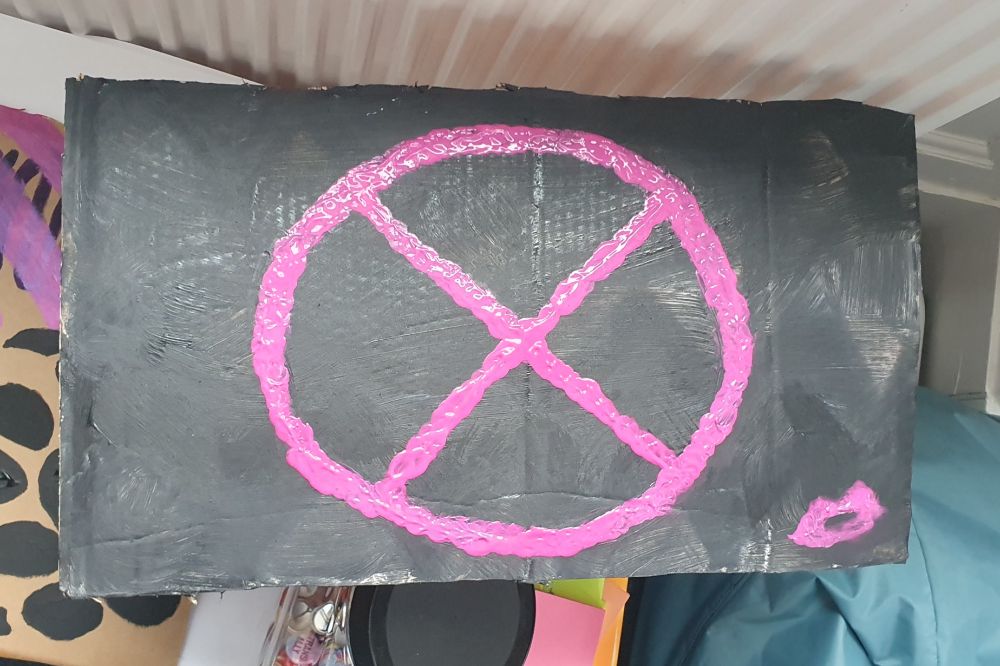 A very basic iteration of the classic X-Men symbol in pink to celebrate the concepts importance to the queer community. There is a shoddily painted kiss, also in pink, next to it.