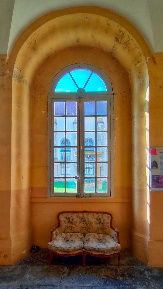 Un petit canapé deux places devant une fenêtre dans un bâtiment ancien en pierre