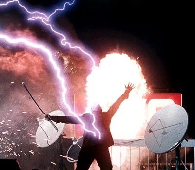 Still of Adrian Paul as Duncan Macleod in the Highlander tv series, backlit by a small explosion/fire caused by the lightning of the Quickening he is taking, which is still shooting into him and also appears to have blown out a couple of 90s satellite dishes. His head is thrown back and his face isn’t really visible; you can really only tell it’s Duncan Macleod bc the carved handle of his katana is visible, held in his outstretched right arm while his left grasps emptily at the sky. He might be wearing all black (pants, shirt, jacket) or that might just be the aforementioned backlighting. 

Side note: Man, if 1990s tailored pants didn’t look good on Adrian Paul, on whom DID they look good?