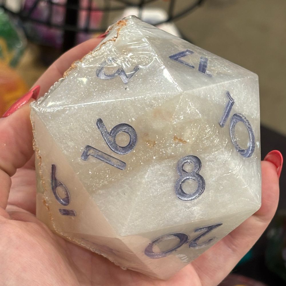 Close up of a giant d20 soap with layers of pearlescent and sparkling white and silver numerals. Through the 8 facet, a white die is visible inside. 
