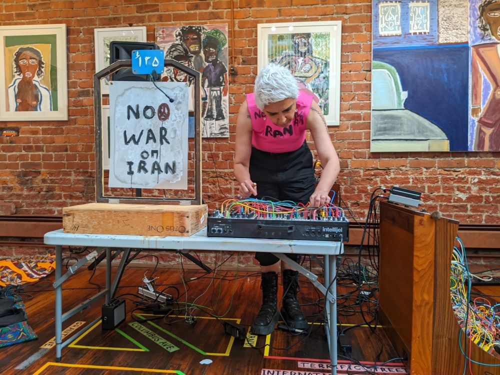 Ava Koohbor performing on modular electronics with resonating metal plate that says "NO WAR ON IRAN"