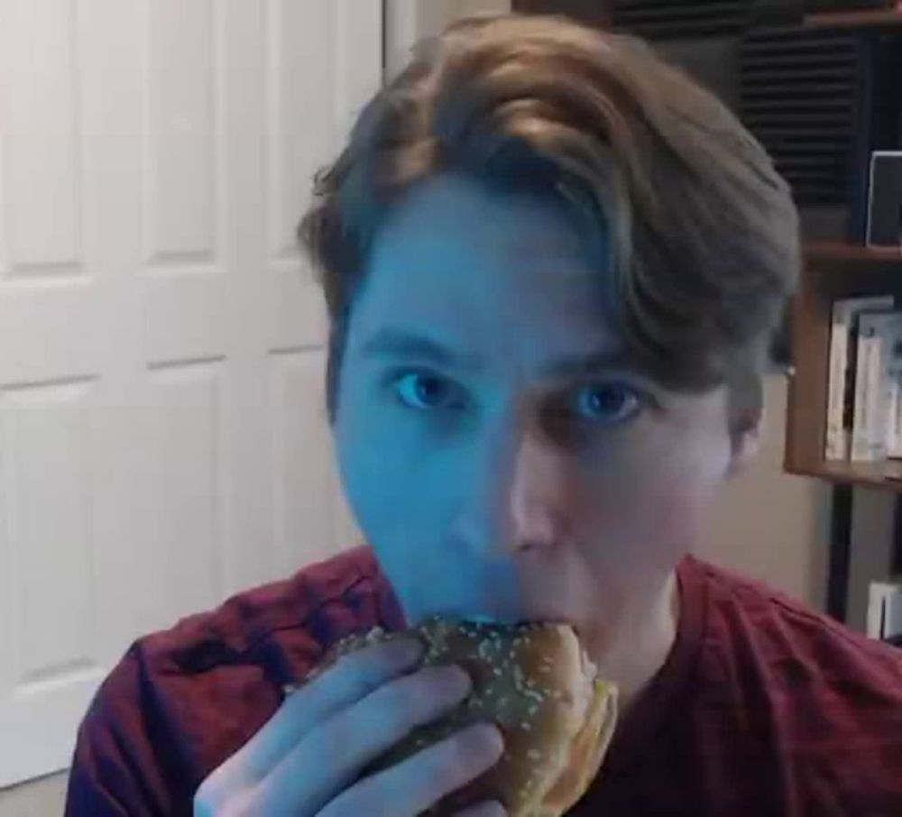 a man is eating a hamburger with sesame seeds on it while looking at the camera .