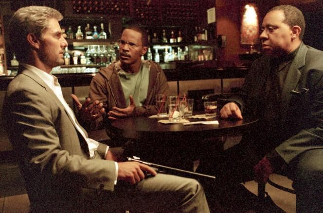 Image du film collatéral de Michael Mann, Tom Cruise, Jamie Foxx et Barry Shabaka Henley attablés dans un bar de jazz. 