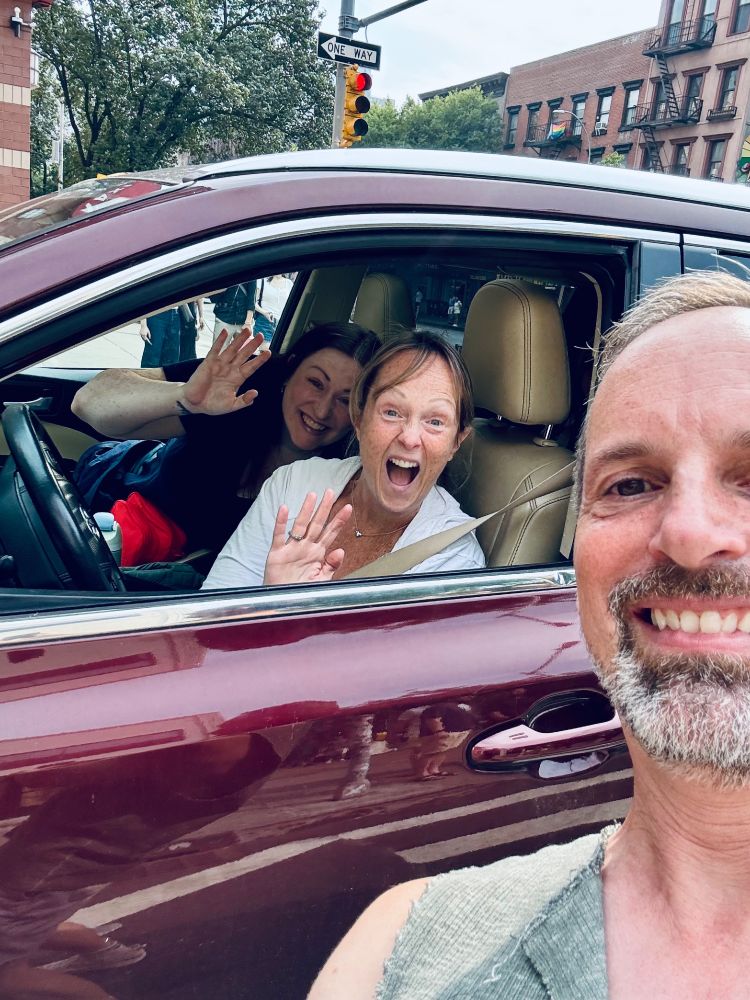 Two women in an SUV wave excitedly for a selfie taken by a guy in the streets of Manhattan - the three of them are cousins who have never met in real life and randomly spotted each other in the streets of Manhattan