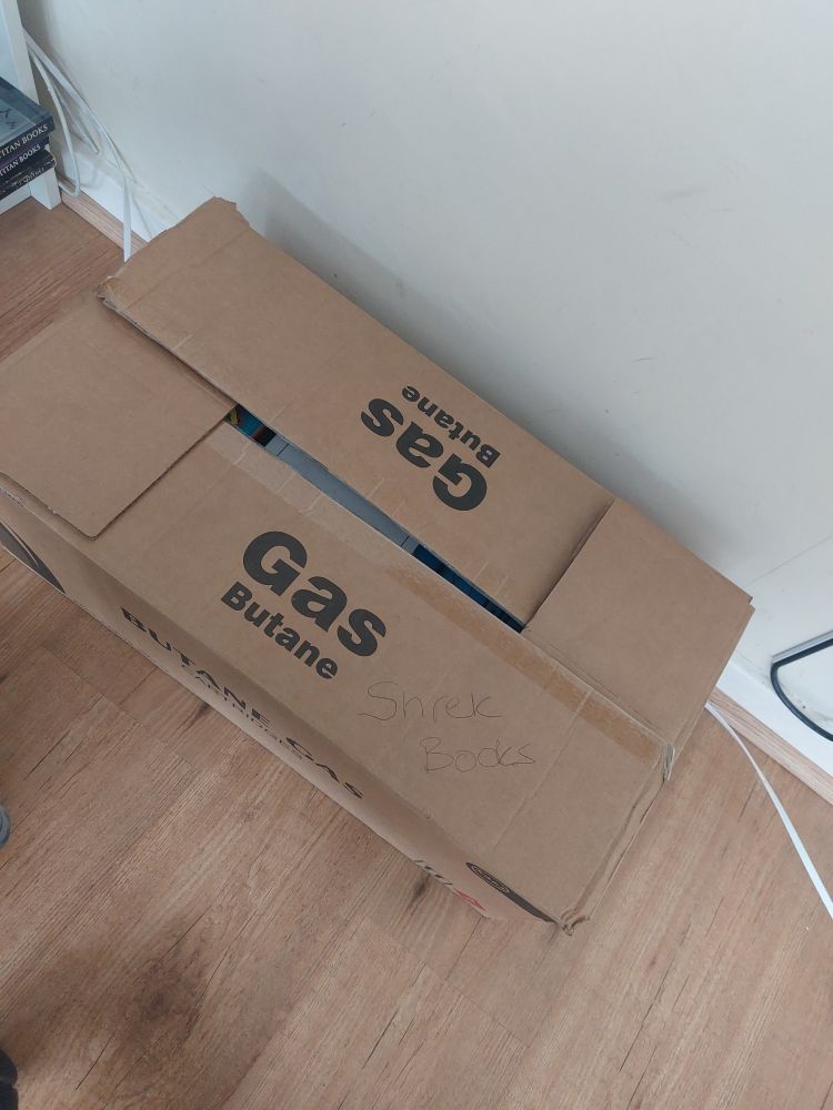 Cardboard box with 'Gas Butane' printed on it and 'Shrek Books' handwritten on it. 