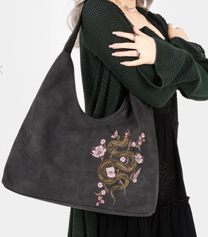 Screenshot from Disturbia clothing website. Model is wearing chunky knit dark green long cardigan. Model is holding large suede black handbag with embroidered snake and floral pattern. Plain white background. 