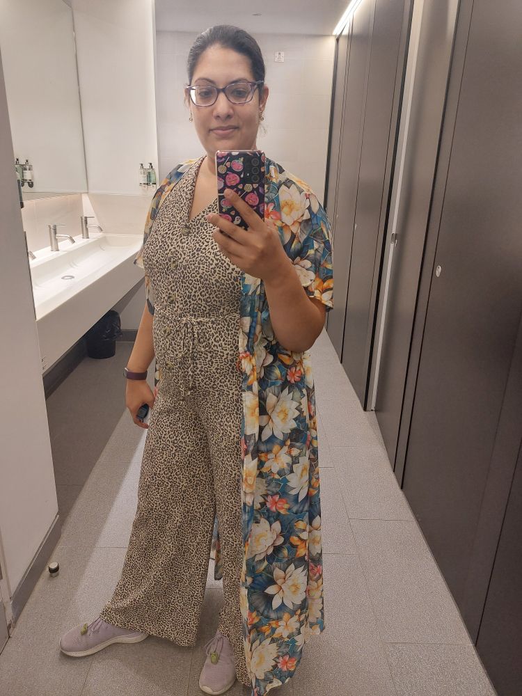 Selfie of me (Indian female with tied up dark brown hair and wearing glasses). Wearing leopard print loose jumpsuit with long floral wrap.