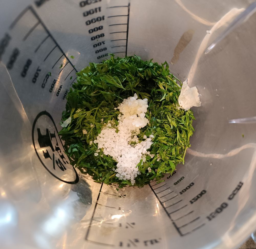 kleingeschnittenes Möhrengrün mit grobem Meersalz und Knoblauch in einem Messbecher