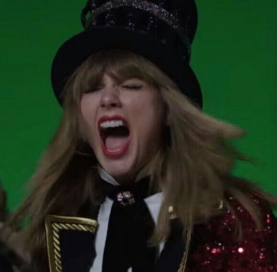 Taylor Swift screaming! Her eyes are closed and her mouth is wide; it’s a loud one. She’s in front of a green screen, wearing the ringmaster costume on the LWYMMD music video set.