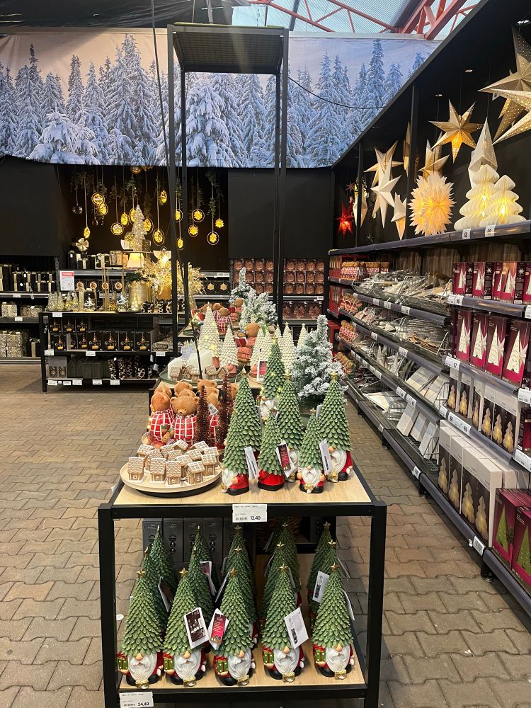 Shelves of Christmas ornaments for the table top, featuring gnomes with Xmas tree hats, tiny replica gingerbread houses, and teddy bears dressed in red checked wrapping.  Plus a variety of hanging stars. 