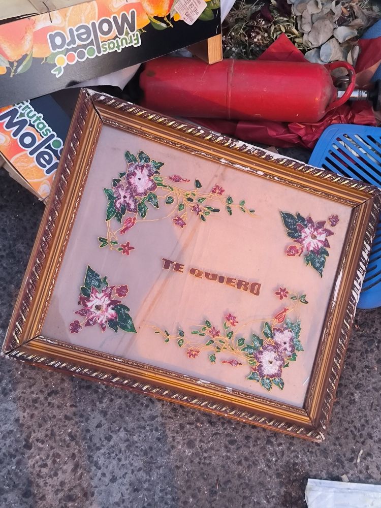 Un cuadro en la basura, con las palabras "Te quiero" sobre fondo de flores.