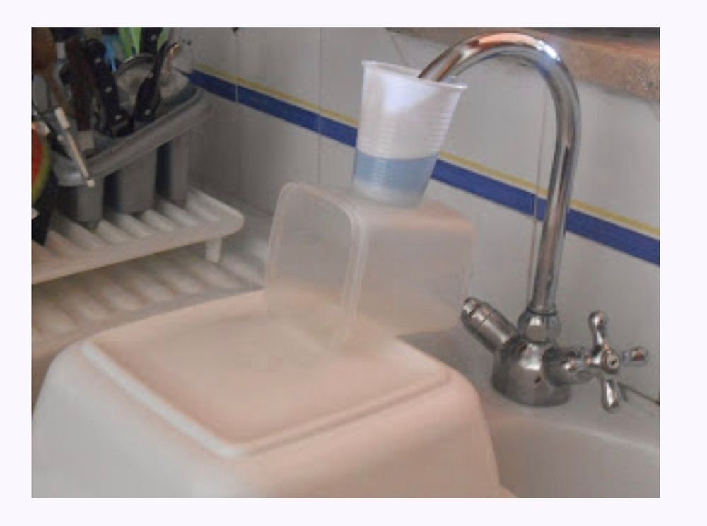 A tap in Rome being descaled. The end of the tap is in a plastic cup on a plastic box on an upturned washing up bowl.