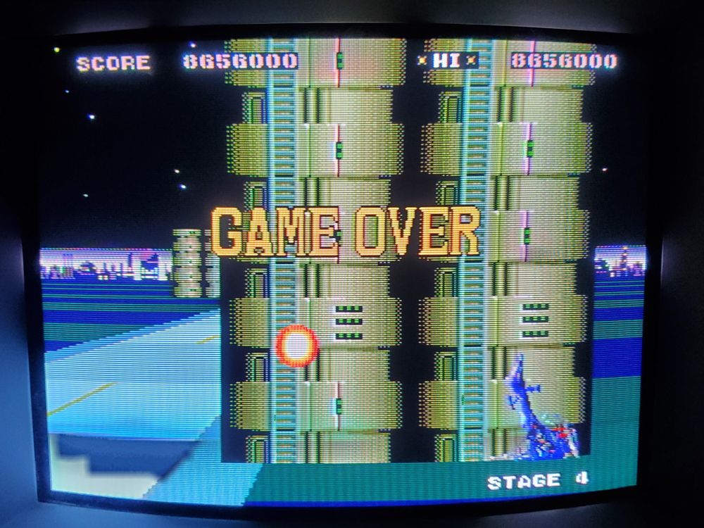 a photo of super thunder blade on sega genesis, photographed on a CRT. the player has just game over'd on the last stage as their helicopter lies in a flaming wreck in front of a building with yellow "GAME OVER" text overlayed in the middle. the final score was 8,656,000 points