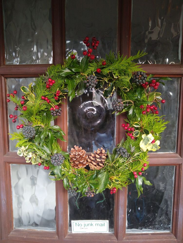 Yule wreath on my front door, covered in conifer branches, holly, ivy, rosemary, lavender and haw berries, with two pine cones tied inside the bottom of the hoop.