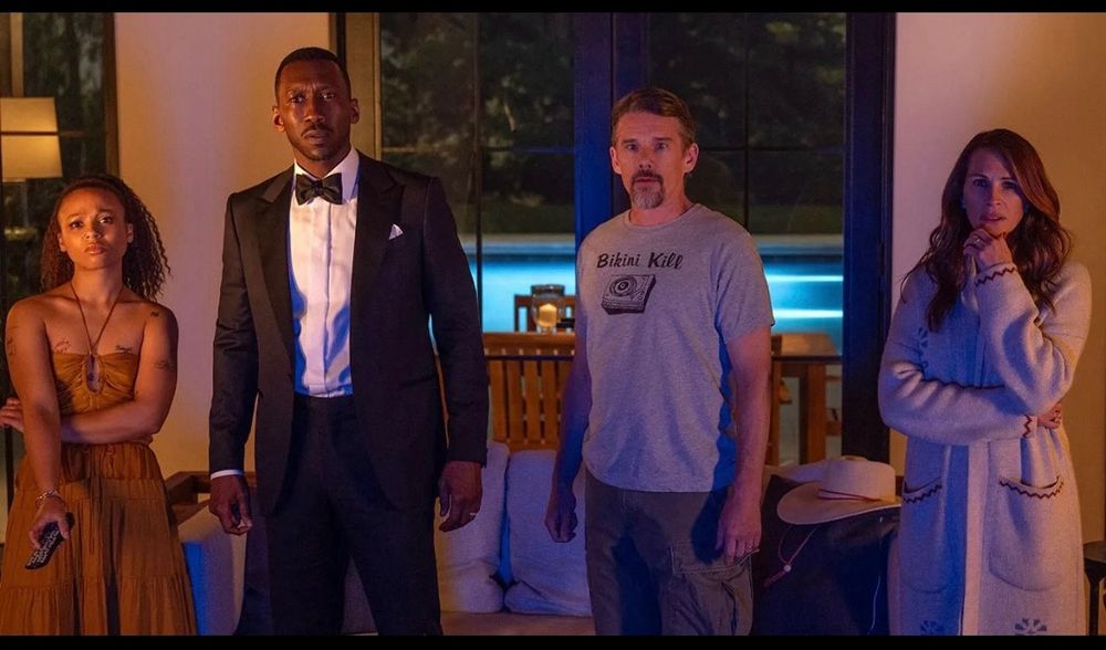 🎥📽️ Scene image from the film ‘Leave The World Behind’ (a Netflix movie directed by Sam Esmail.) The image depicts Julia Roberts, Myha’la, Ethan Hawke, and Mahershala Ali all staring at the tv in bewilderment as they watch the news explaining that America is under attack (via complete cell tower outages, all airplanes crashing, and total abandonment by the US government.)