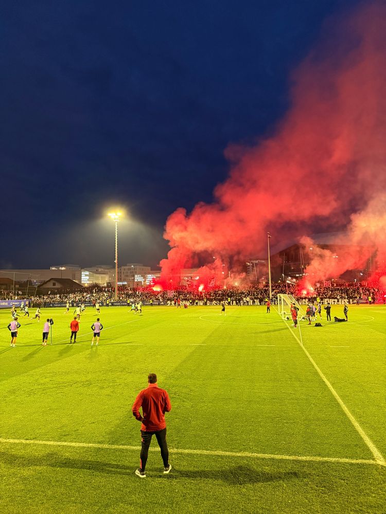 Séance d’entraînement de l’Olympique Lyonnais la veille du Derby. Dans le fond, les supporters du clubs de Lyon utilisent des fumigènes rouges. 