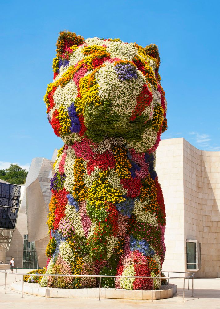 "Puppy", a sculpture by artist Jeff Koons. 43 feet tall.

The beautifully colorful floral sculpture is formed from a series of stainless steel armatures constructed to hold over 25 tons of soil watered by an internal irrigation system. 

Over 70,000 multi-hued flowering plants grow from this steel and soil structure, including marigolds, begonias, impatiens, petunias, and lobelias. First created in 1992 for a temporary exhibition in the German city of Arolson, Puppy—a symbol, according to Koons, of “love, warmth and happiness”—embodies the artist’s sculptural imagination.