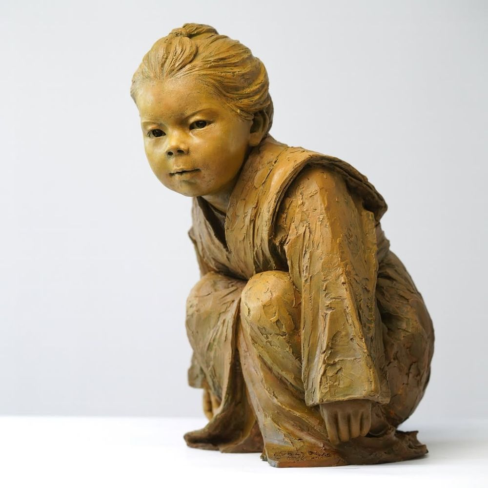 Artist Luo Li Rong's bronze sculpture "Gaze of Childhood", which depicts a crouching child wearing a robe. "This sculpture emphasizes the child’s focused expression, aiming to convey the natural, quiet, and attentive moments of childhood. The posture and facial expression of the figure reflect the subtle interaction between the child and their surroundings, as if exploring the world around them, with a touch of innocence and curiosity"