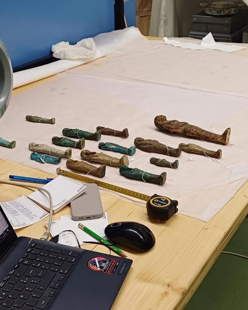 Ouchebtis disposés sur un bureau à côté d’un ordinateur.