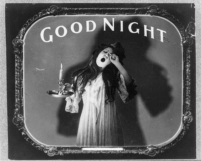 yawning woman in night dress with a lit candle in candle holder heads off for a sleep