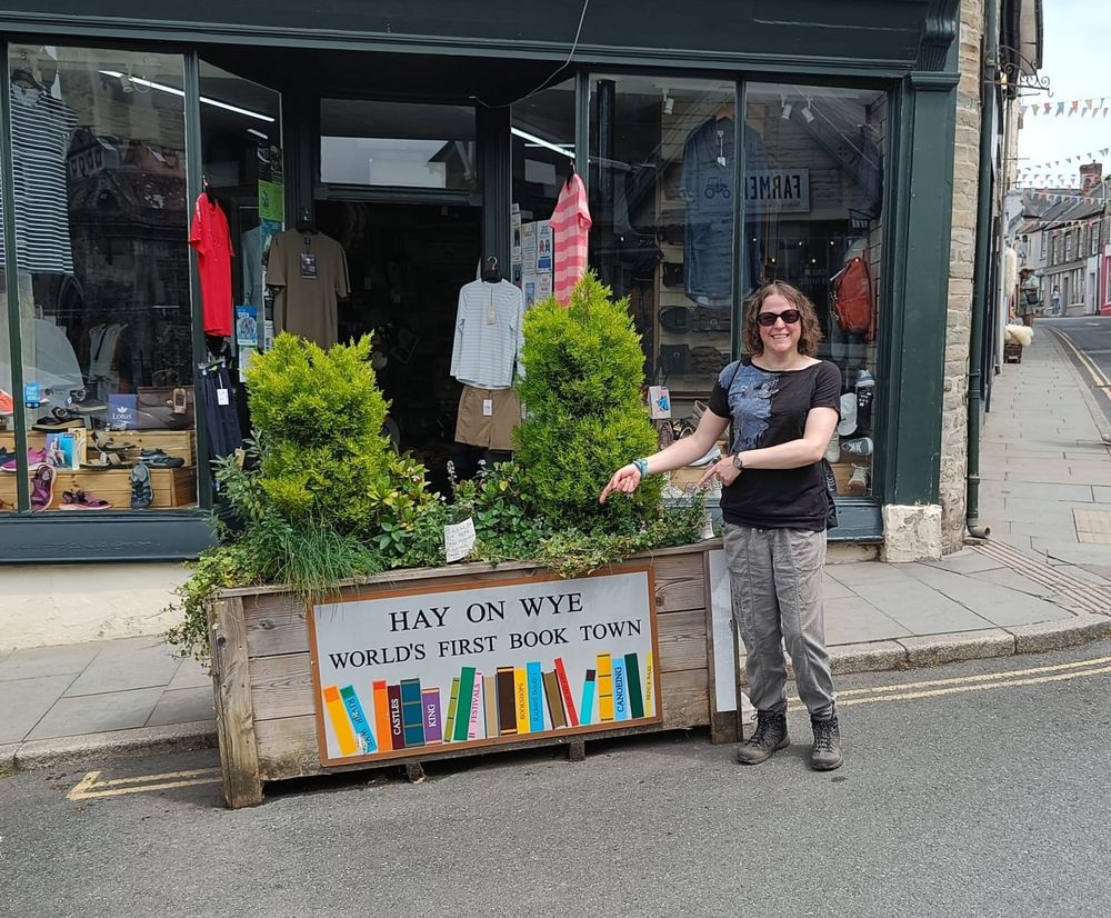 Photo of a person pointing to a sign saying Hay on Wye World's First Book Town.
