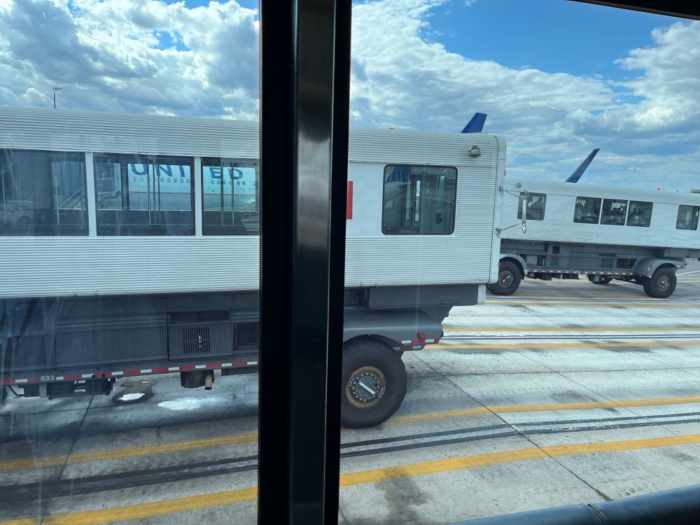 View out a window at two people mover vehicles in their bays at the terminal. They’re like big train compartments set on four wheels. One is sitting empty, the second is rolling down the ramp on its way.